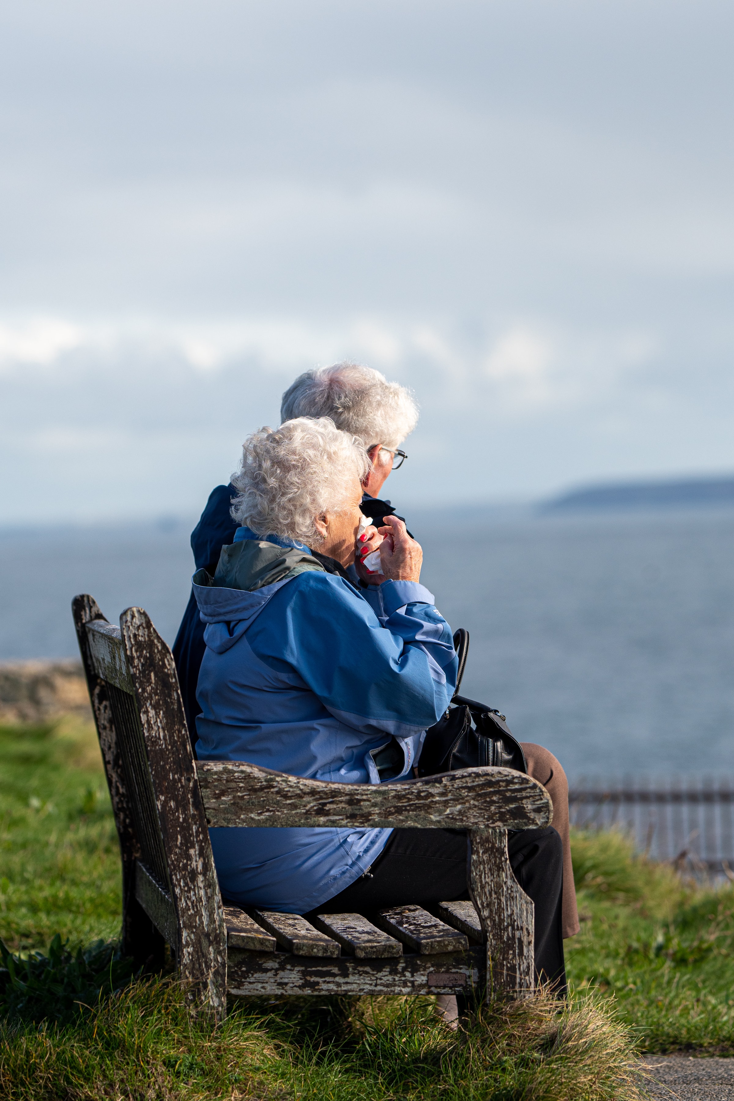 An elderly couple seating on a bench, overlooking the sea